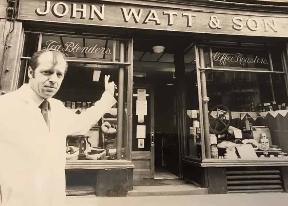 Black and white photograph of a man standing outside John Watt & Son coffee roasters in Carlisle